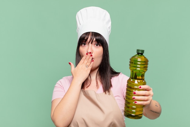 Mujer bonita chef expresión asustada y sosteniendo una botella de aceite de oliva