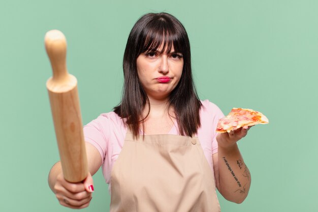 Mujer bonita chef expresión enojada y sosteniendo una pizza