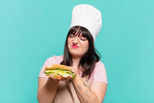 Mujer bonita chef expresión enojada y sosteniendo un sándwich