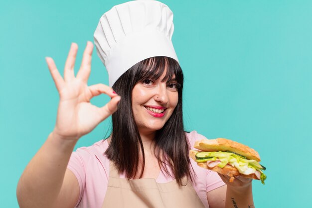 Mujer bonita chef expresión feliz y sosteniendo un sándwich