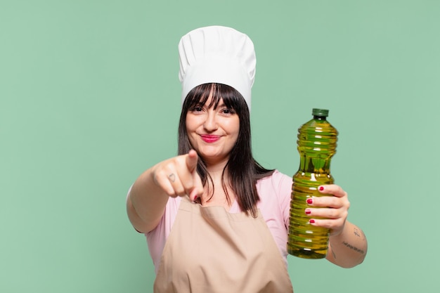 Mujer bonita chef señalando o mostrando y sosteniendo una botella de aceite de oliva