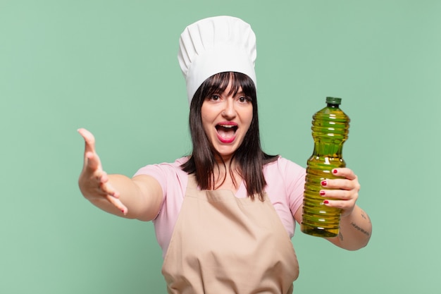 Mujer bonita chef sorprendida expresión y sosteniendo una botella de aceite de oliva