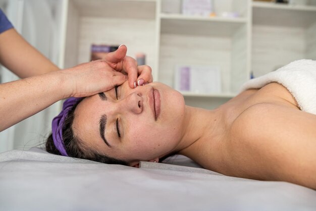 Mujer bonita disfrutando de un masaje facial con los ojos cerrados en el salón de belleza