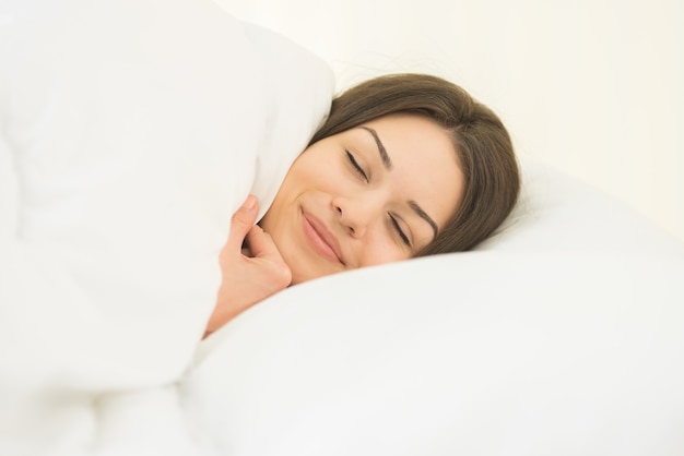 La mujer bonita durmiendo en las sábanas blancas