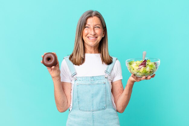 Mujer bonita de edad ociosa con un donut y un concepto de dieta de ensalada