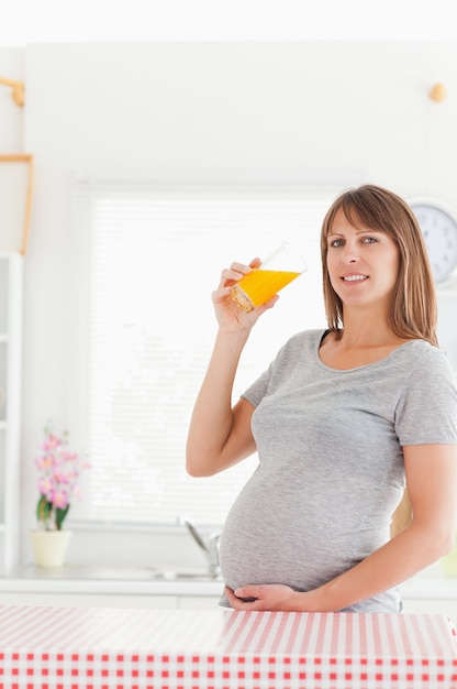 Mujer bonita embarazada bebiendo un vaso de jugo de naranja mientras está de pie