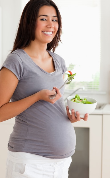 Mujer bonita embarazada sosteniendo un plato de ensalada mientras está de pie