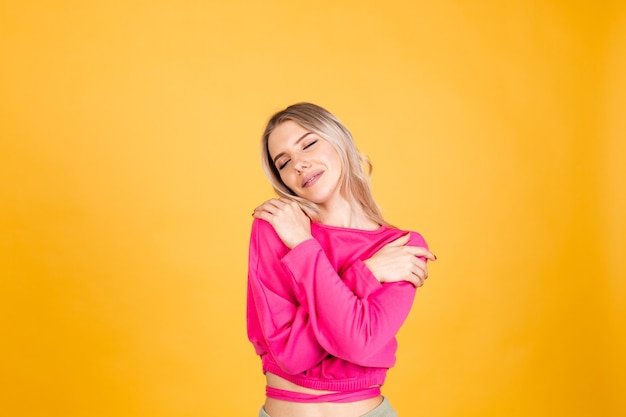 Mujer bonita europea en blusa rosa sobre pared amarilla