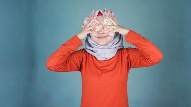 Mujer bonita feliz con hiyab escondiéndose detrás de un montón de billetes de dinero