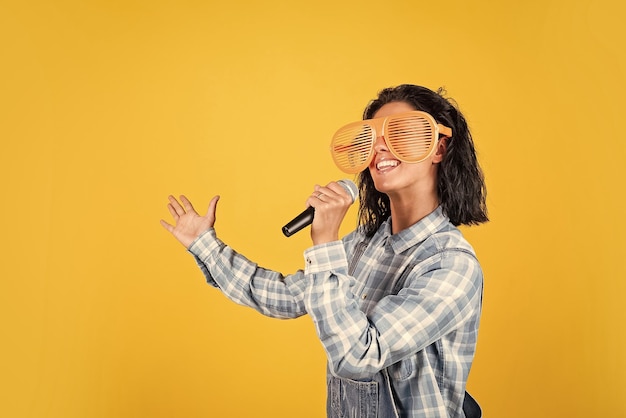 Una mujer bonita feliz con el pelo moreno usa ropa informal y canta una canción en el karaoke del micrófono