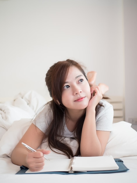 mujer bonita feliz y relajarse para escribir un diario en su cama