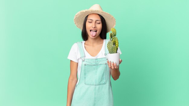 Mujer bonita granjera con actitud alegre y rebelde, bromeando y sacando la lengua y sosteniendo un cactus