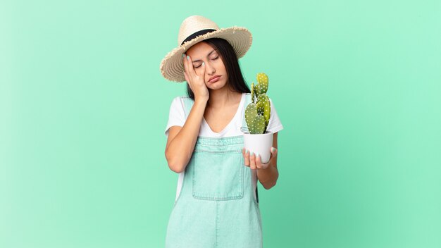 Mujer bonita granjera que se siente aburrida, frustrada y con sueño después de un cansado y sosteniendo un cactus