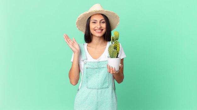 Mujer bonita granjera que se siente feliz, sorprendida al darse cuenta de una solución o idea y sosteniendo un cactus