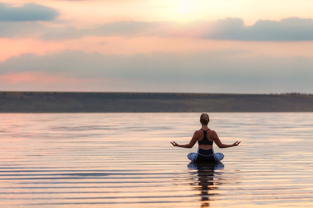 La mujer bonita haciendo yoga al atardecer al aire libre