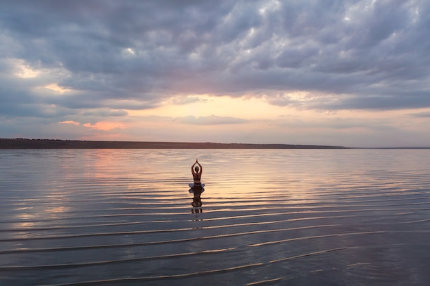 La mujer bonita haciendo yoga al atardecer al aire libre