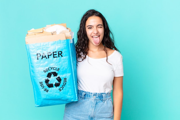 Mujer bonita hispana con actitud alegre y rebelde, bromeando y sacando la lengua y sosteniendo una bolsa de papel reciclado