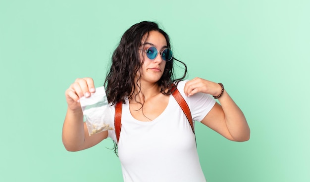 Mujer bonita hispana de aspecto arrogante, exitoso, positivo y orgulloso y sosteniendo una bolsa de marihuana