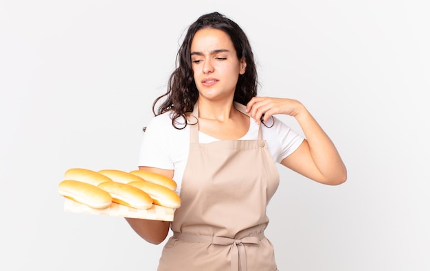 Mujer bonita hispana chef sintiéndose estresada, ansiosa, cansada y frustrada y sosteniendo un pan troy