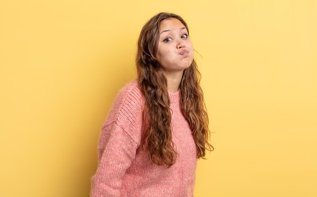 Mujer bonita hispana con una expresión tonta, loca, sorprendida, hinchando las mejillas, sintiéndose rellena, gorda y llena de comida