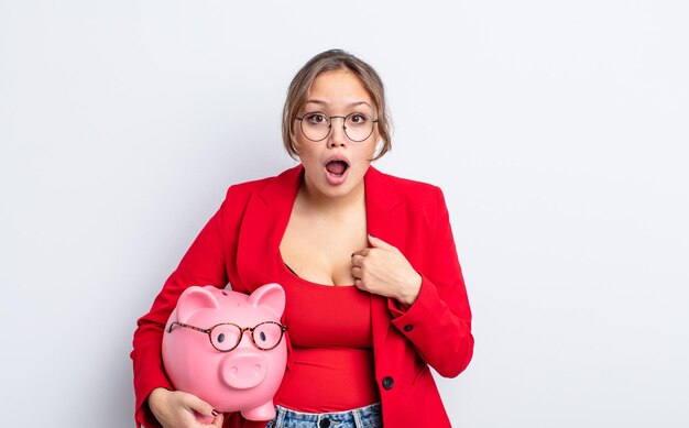 Mujer bonita hispana mirando consternado y sorprendido con la boca abierta, apuntando a sí mismo. concepto de alcancía