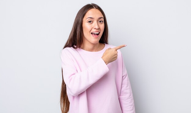 Mujer bonita hispana mirando emocionada y sorprendida apuntando hacia un lado y hacia arriba para copiar el espacio