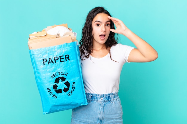 Mujer bonita hispana mirando feliz, asombrado y sorprendido y sosteniendo una bolsa de papel reciclado