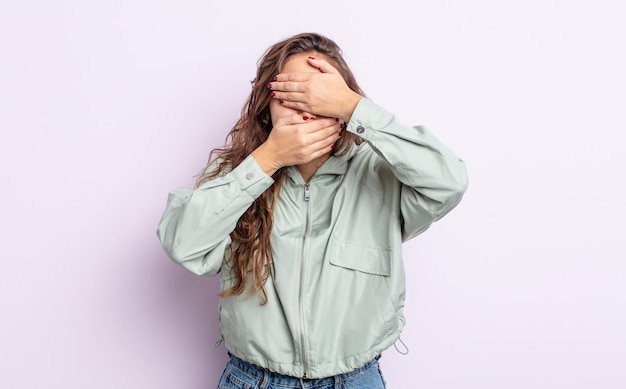 ¡Mujer bonita hispana que cubre la cara con ambas manos diciendo no a la cámara! rechazar fotografías o prohibir fotografías