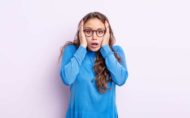 Mujer bonita hispana que parece desagradablemente sorprendida, asustada o preocupada, con la boca abierta y cubriendo ambos oídos con las manos