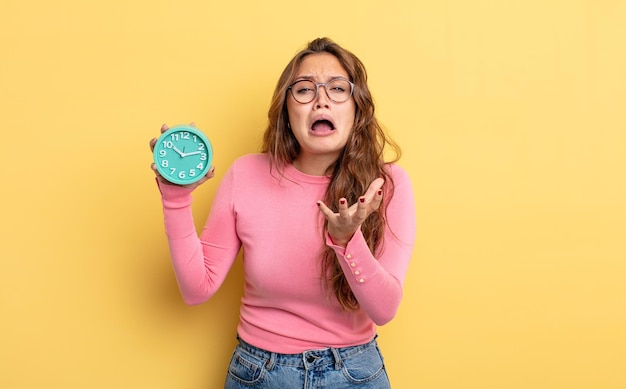 Mujer bonita hispana que parece desesperada, frustrada y estresada. concepto de reloj despertador