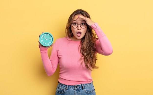 Mujer bonita hispana que parece feliz, asombrada y sorprendida. concepto de reloj despertador