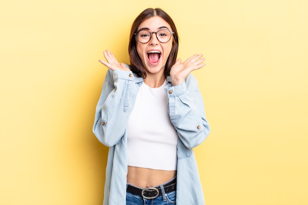 Mujer bonita hispana que parece feliz y emocionada, sorprendida con una sorpresa inesperada con ambas manos abiertas junto a la cara