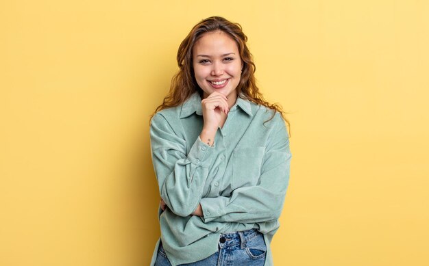 Mujer bonita hispana que parece feliz y sonriente con la mano en la barbilla, preguntándose o haciendo una pregunta, comparando opciones