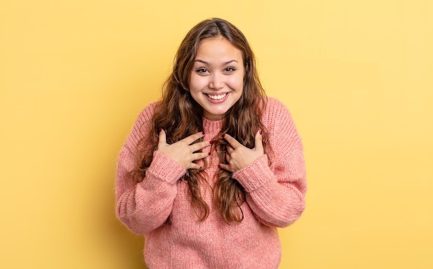 Mujer bonita hispana que parece feliz, sorprendida, orgullosa y emocionada, apuntándose a sí misma