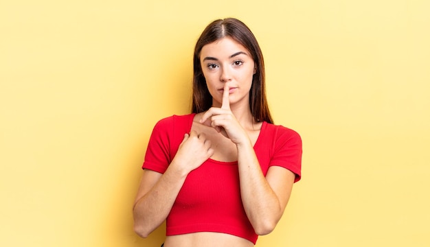 Mujer bonita hispana que parece seria y cruzada con el dedo presionado en los labios exigiendo silencio o silencio guardando un secreto