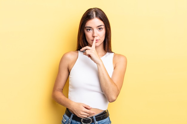 Mujer bonita hispana que parece seria y cruzada con el dedo presionado a los labios exigiendo silencio o silencio, manteniendo un secreto