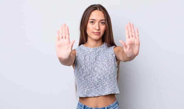 Mujer bonita hispana que parece seria, infeliz, enojada y disgustada prohibiendo la entrada o diciendo que pare con ambas palmas abiertas