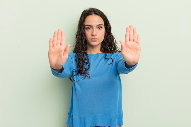 Mujer bonita hispana que parece seria, infeliz, enojada y disgustada, que prohíbe la entrada o dice que se detenga con ambas palmas abiertas