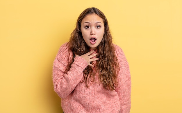 Mujer bonita hispana que se siente conmocionada, asombrada y sorprendida, con la mano en el pecho y la boca abierta, diciendo quién, ¿yo?