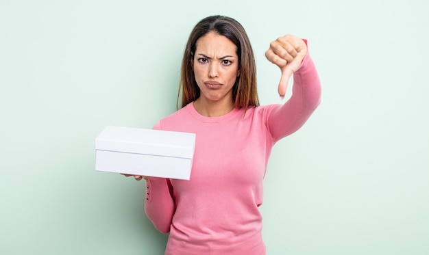 Mujer bonita hispana que se siente cruzada, mostrando los pulgares hacia abajo. concepto de embalaje de caja blanca