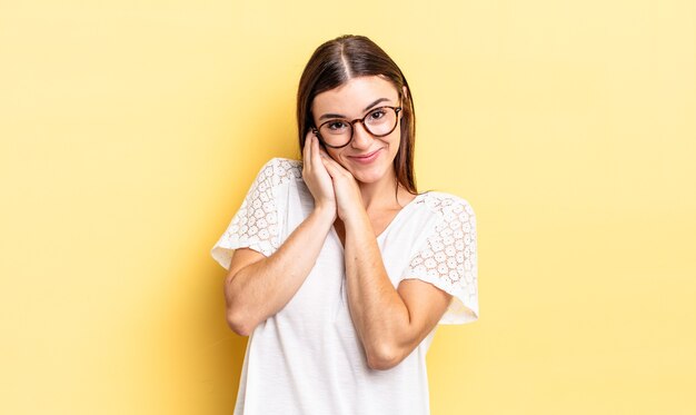 Mujer bonita hispana que se siente enamorada y se ve linda, adorable y feliz, sonriendo románticamente con las manos al lado de la cara