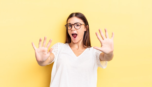 Mujer bonita hispana que se siente estupefacta y asustada, por miedo a algo aterrador, con las manos abiertas al frente diciendo que se mantenga alejado