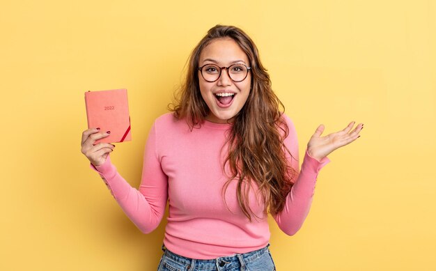 Mujer bonita hispana que se siente feliz y asombrada por algo increíble. concepto de agenda