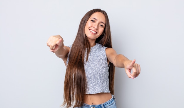 Mujer bonita hispana que se siente feliz y confiada, apuntando a la cámara con ambas manos y riendo, eligiéndote