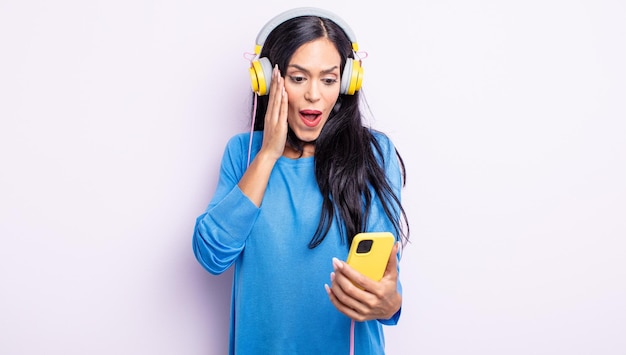 Mujer bonita hispana que se siente feliz, emocionada y sorprendida. concepto de teléfono inteligente y auriculares