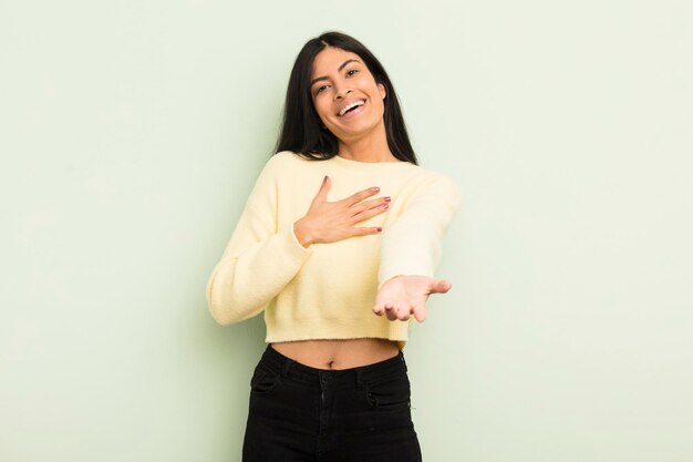 Mujer bonita hispana que se siente feliz y enamorada sonriendo con una mano al lado del corazón y la otra estirada al frente