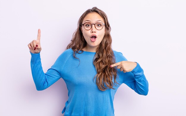 Mujer bonita hispana que se siente orgullosa y sorprendida, apuntando a sí misma con confianza, sintiéndose como el número uno exitoso