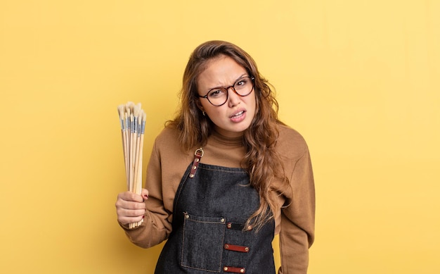 Mujer bonita hispana que se siente perpleja y confundida. artista con concepto de pinceles