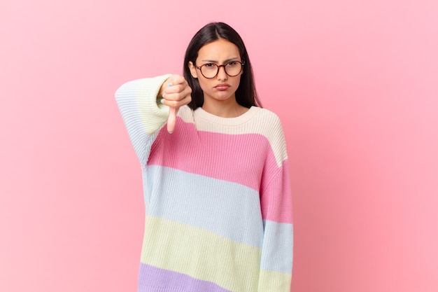 Mujer bonita hispana sentimiento cruzado, mostrando los pulgares hacia abajo