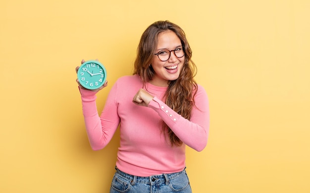 Mujer bonita hispana sintiéndose feliz y enfrentando un desafío o celebrando. concepto de reloj despertador